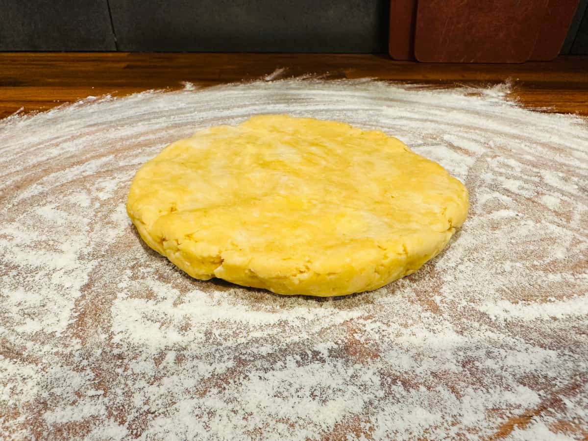 Disk of butter crust dough sitting on a floured wood surface.
