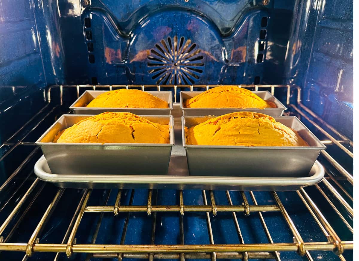Four miniature loaves of pumpkin bread baking in a blue oven.