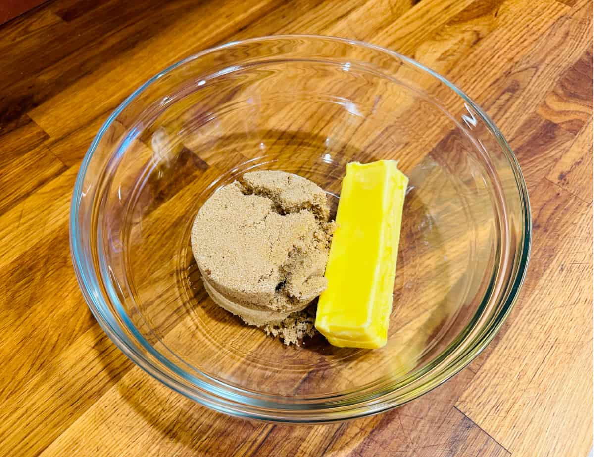 Light brown sugar and a cube of butter in a glass bowl.