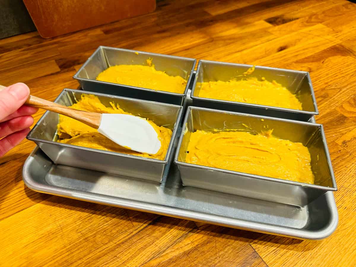 Four miniature loaf pans filled with pumpkin bread batter.