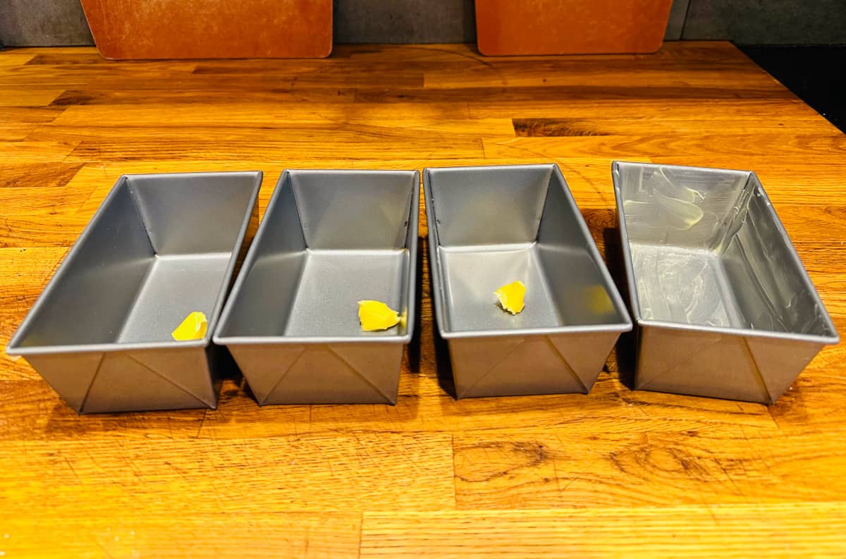 Four miniature loaf pans with butter in them.