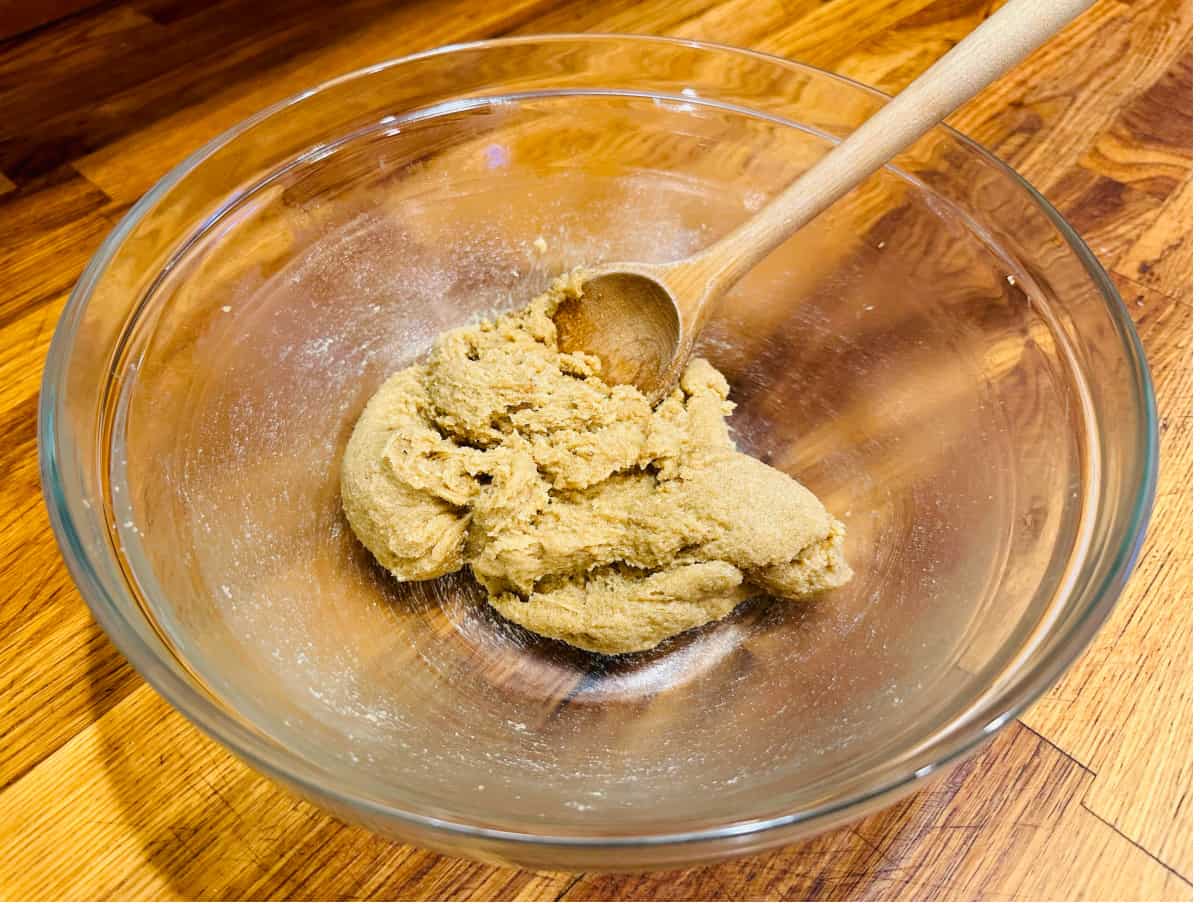 Mixture of butter and sugar in a glass bowl with a wooden spoon.
