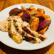 Slices of roasted chicken with roasted carrots, potatoes, yam, and red onion on a white plate.
