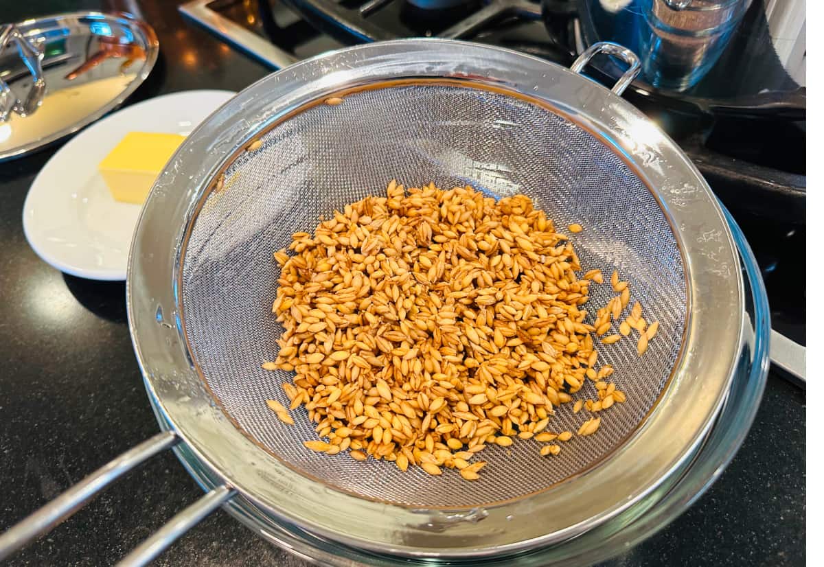 Raw barley in a metal strainer.