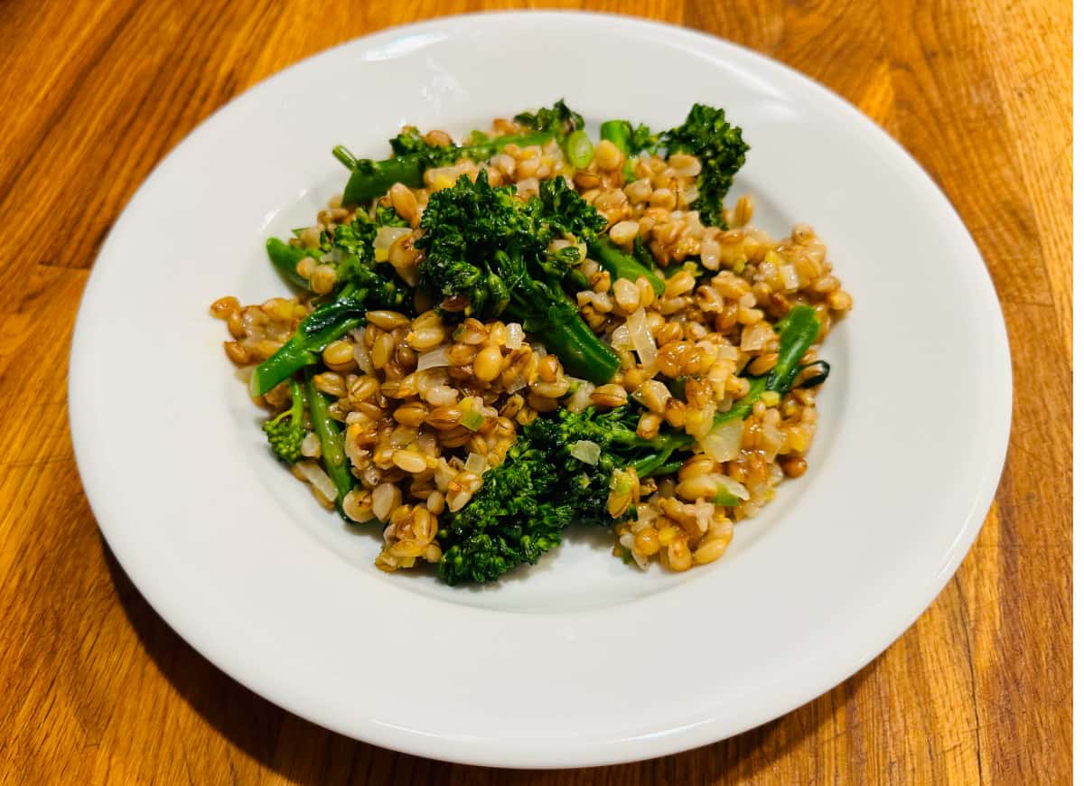 Barley pilaf with broccolini in a shallow white bowl.