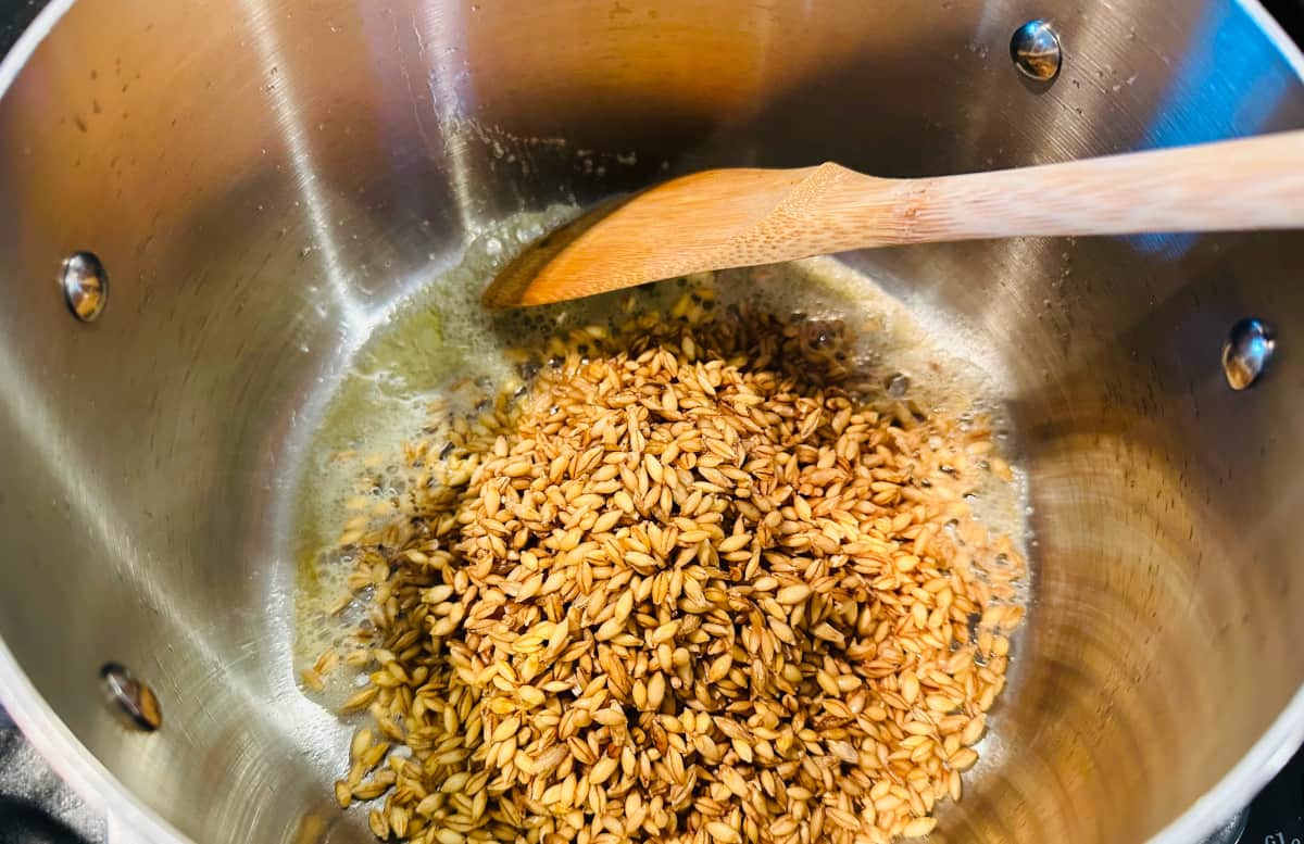 Barley toasting in butter in a metal pot.