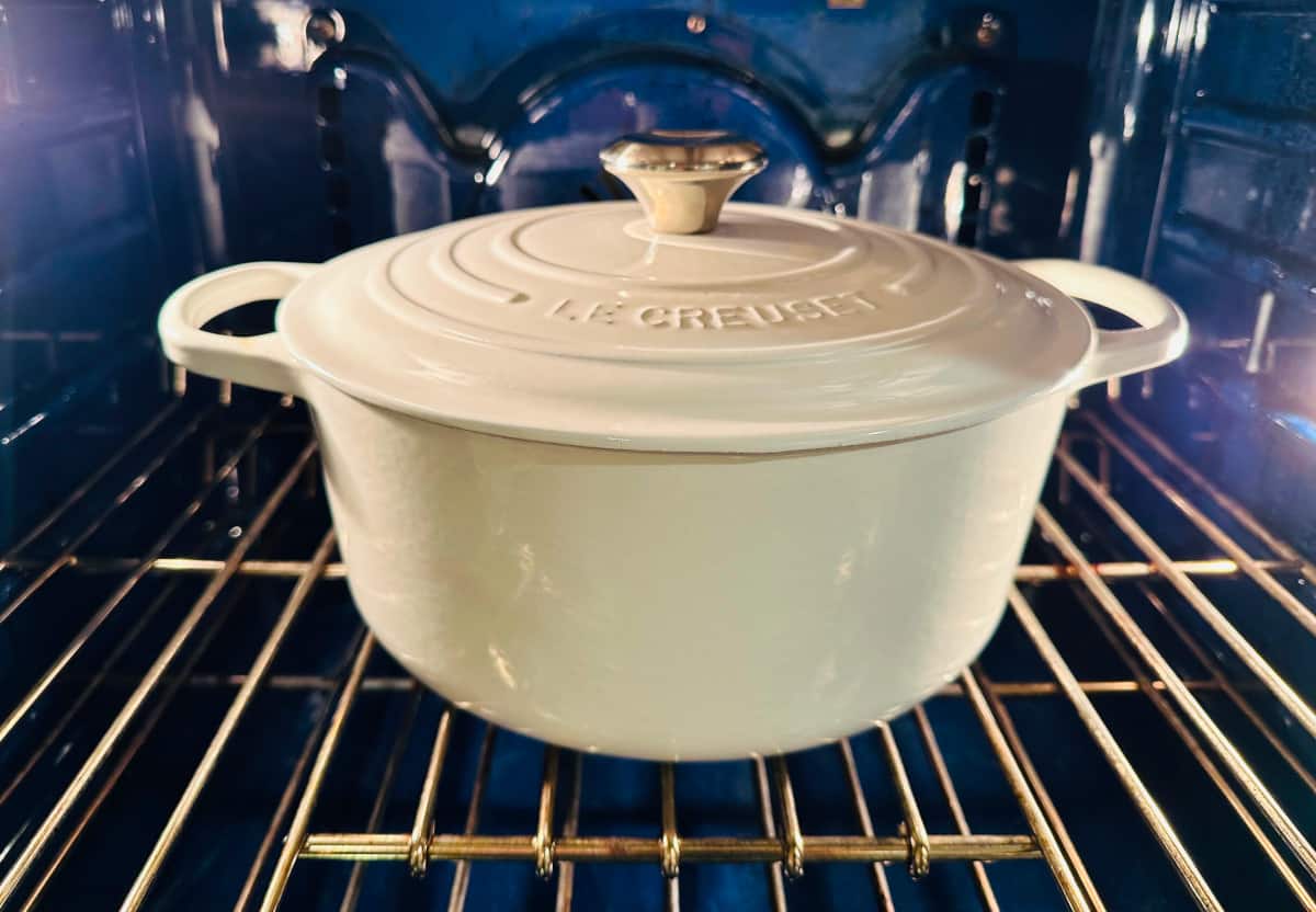 White pot covered with a lid sitting on a rack in a blue oven.