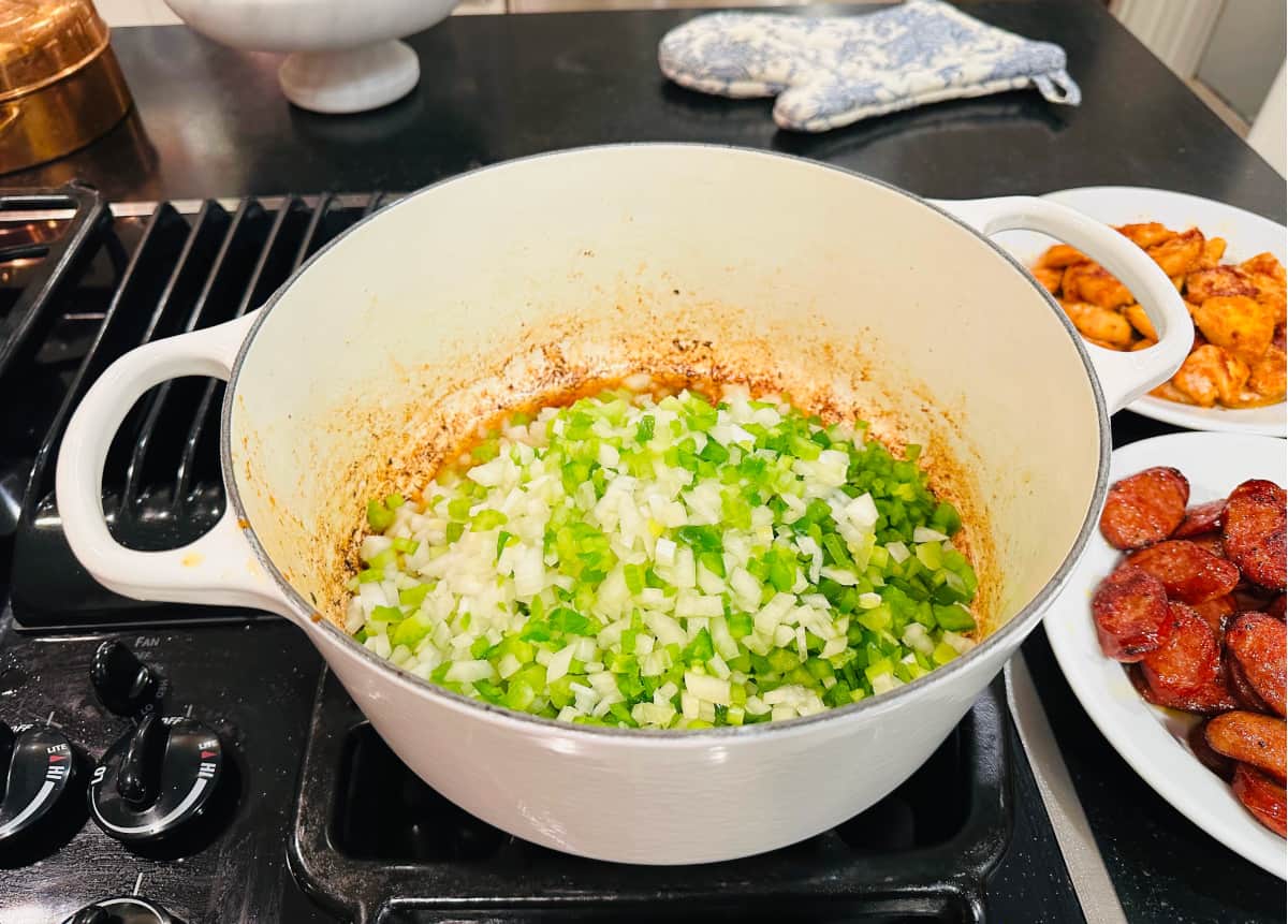 Chopped onion, celery, and green pepper cooking in a white pot.