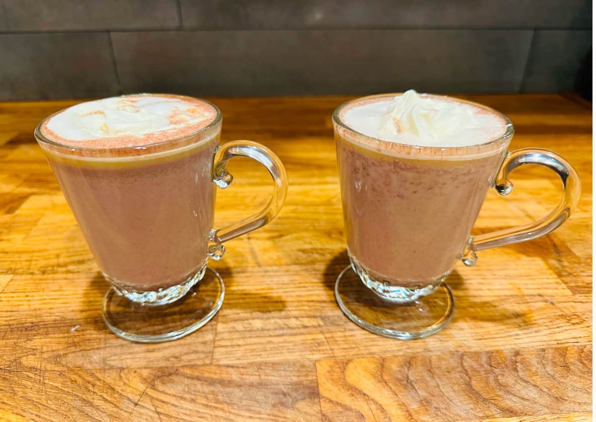 Two glass mugs of Spanish hot chocolate sitting on a butcher block counter.