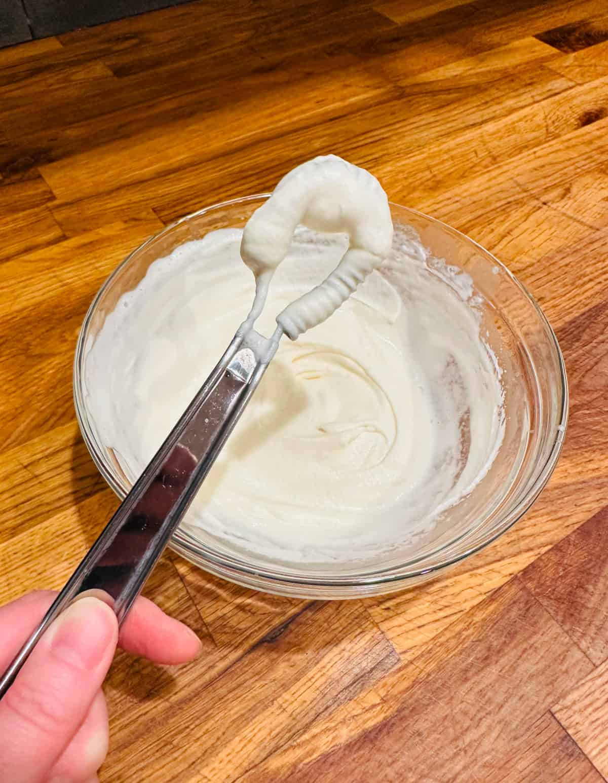 A hand holding a magic whisk over a small glass bowl of whipped cream.