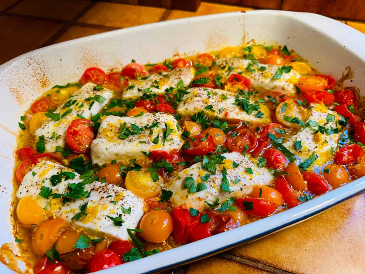 Halibut provencal garnished with chopped parsley in a white baking dish.