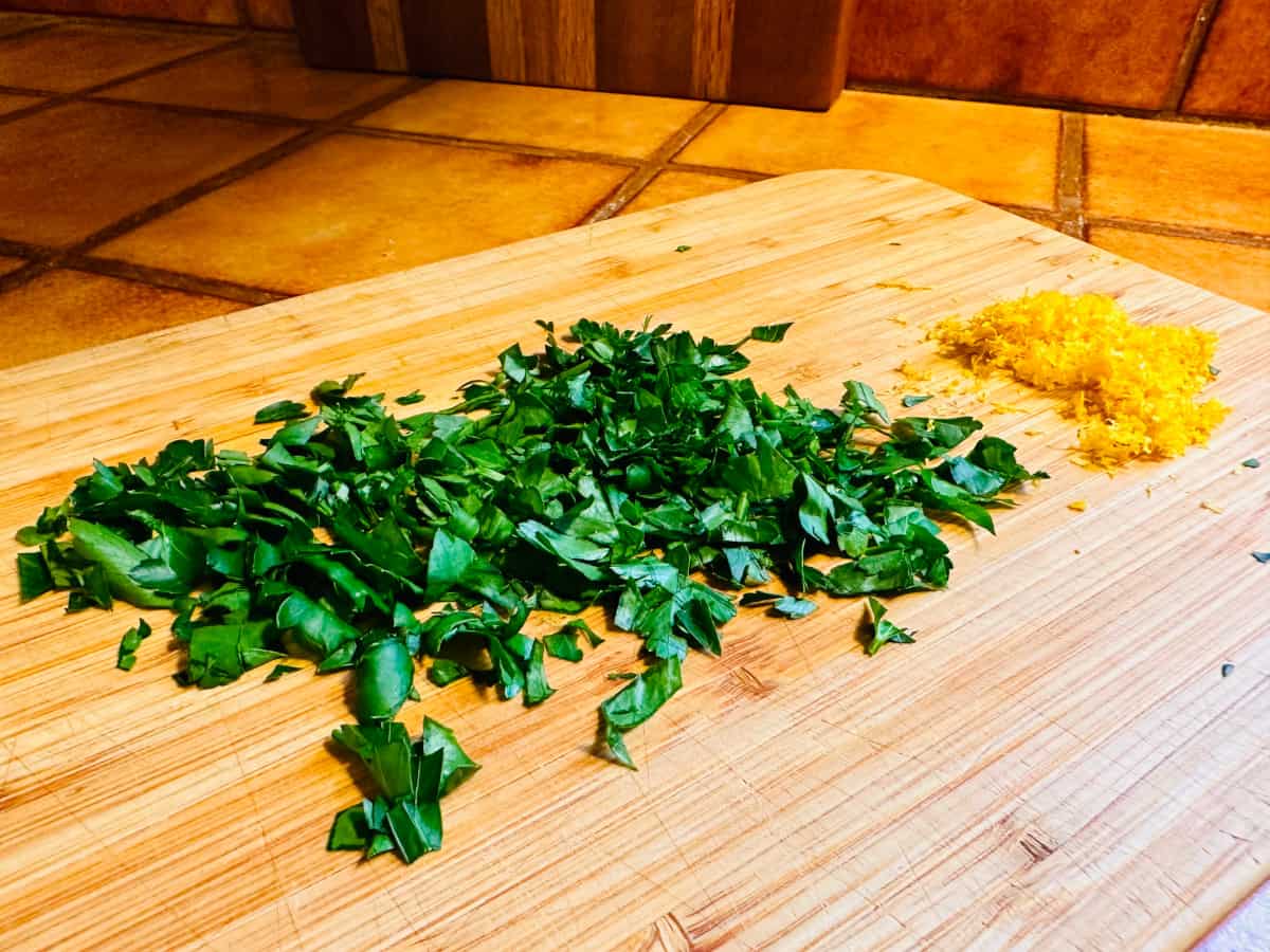 A large pile of chopped parsley and a small pile of lemon zest on a cutting board.