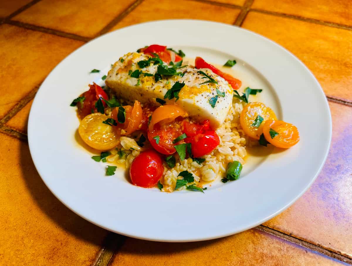 Halibut provencal served over rice on a white plate.
