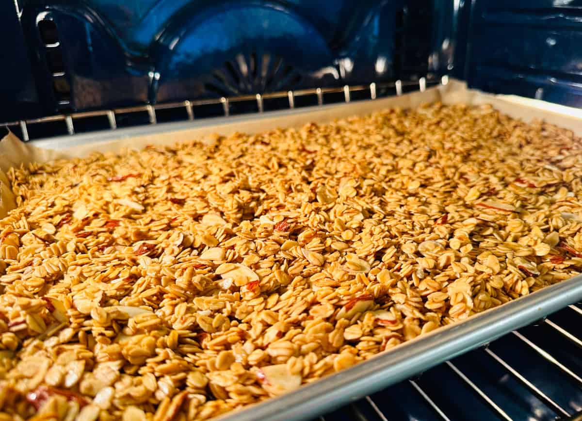 Granola baking on a metal baking sheet in a blue oven.