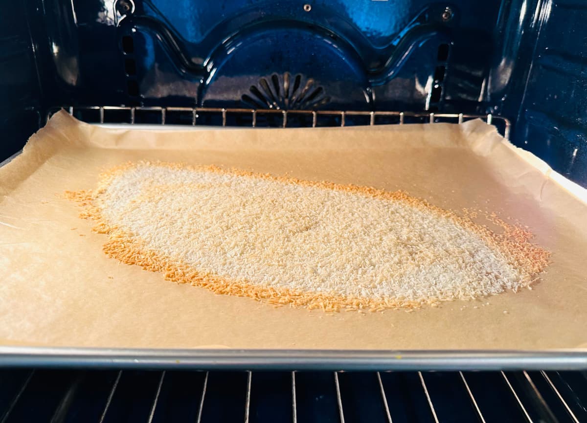 Shredded coconut toasting in a blue oven on a metal baking sheet covered with parchment paper.
