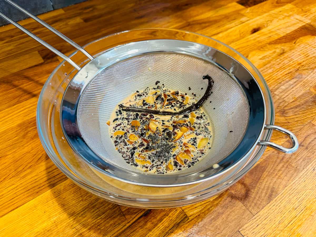 Flavorings for Irish Cream sitting in a metal strainer set on top of a glass bowl containing tan liquid.