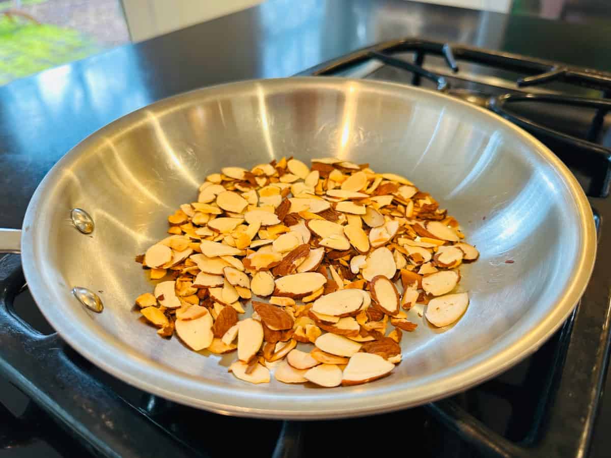 Sliced almonds toasting in a small metal frying pan.