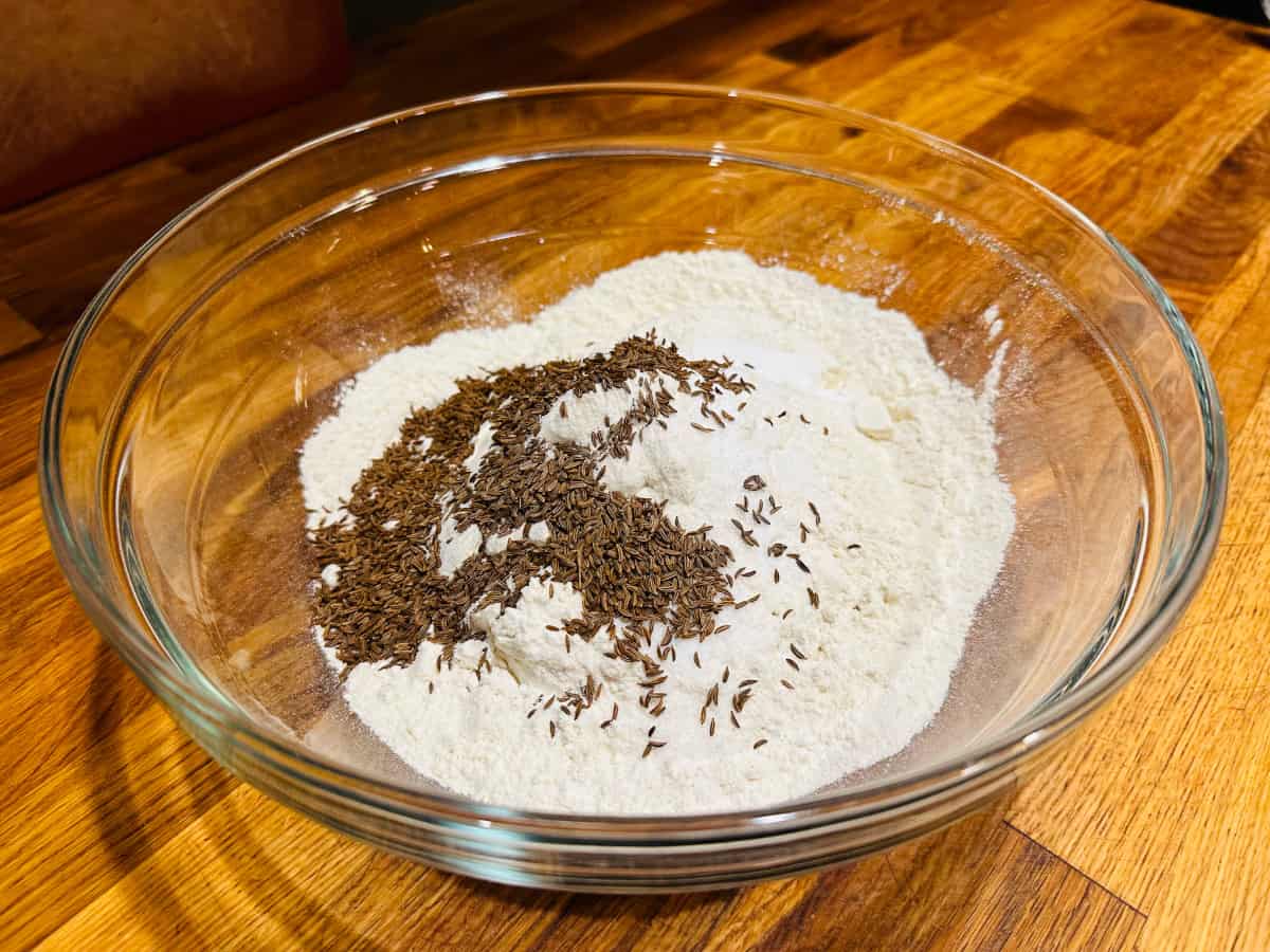 Flour, baking soda, salt, and caraway seeds in a glass bowl.