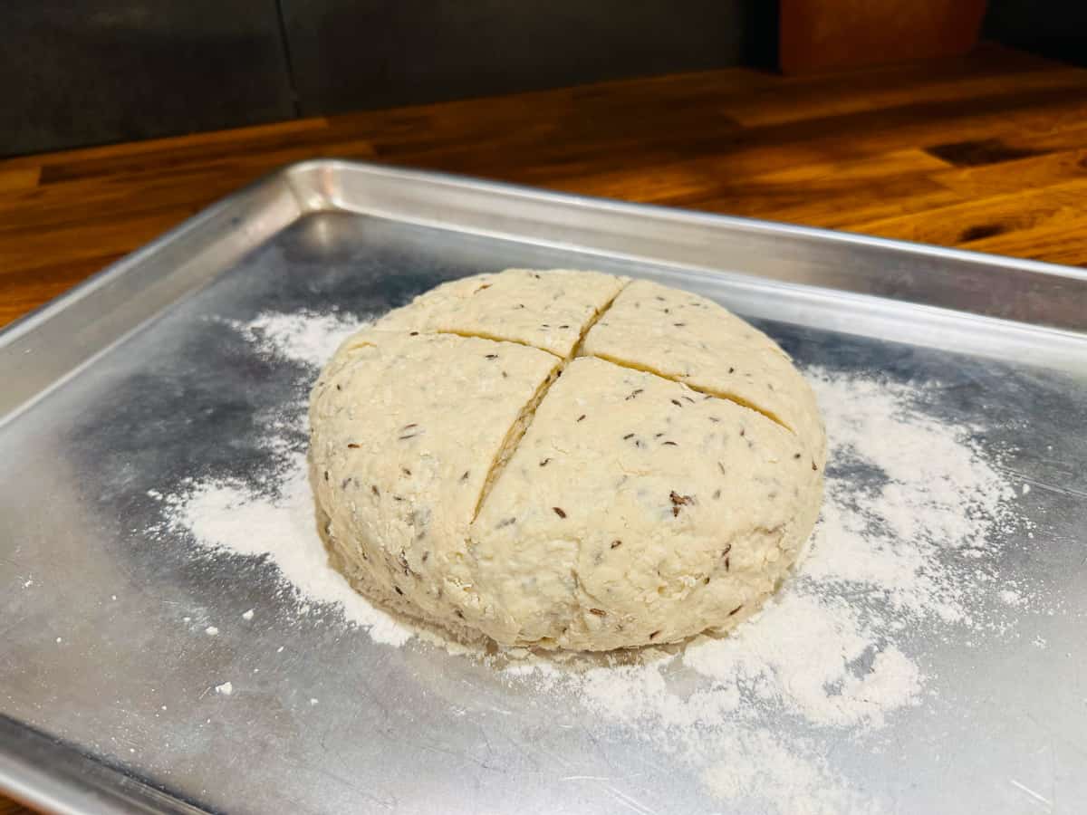 Unbaked loaf of Irish soda bread on a lightly floured metal baking sheet.
