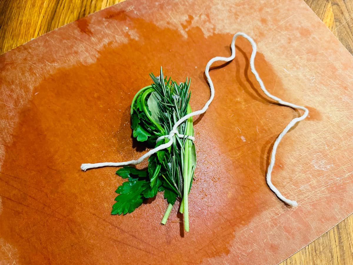 Sprigs of parsley, rosemary, and a bay leaf tied up in a bundle with white butcher's twine.