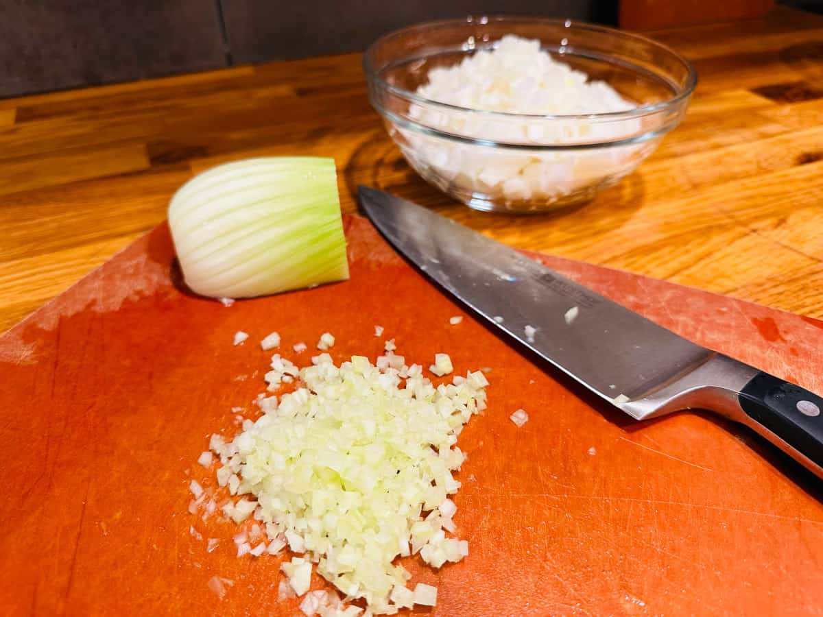 Minced fennel and a fennel bulb with a knife on a cutting board.
