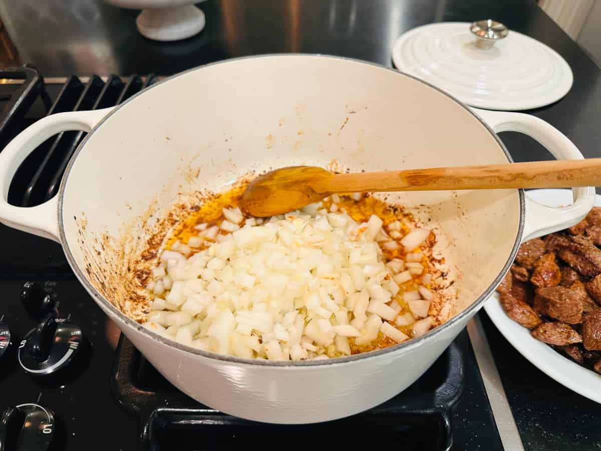 Chopped onions in a white pot with a wooden spoon.