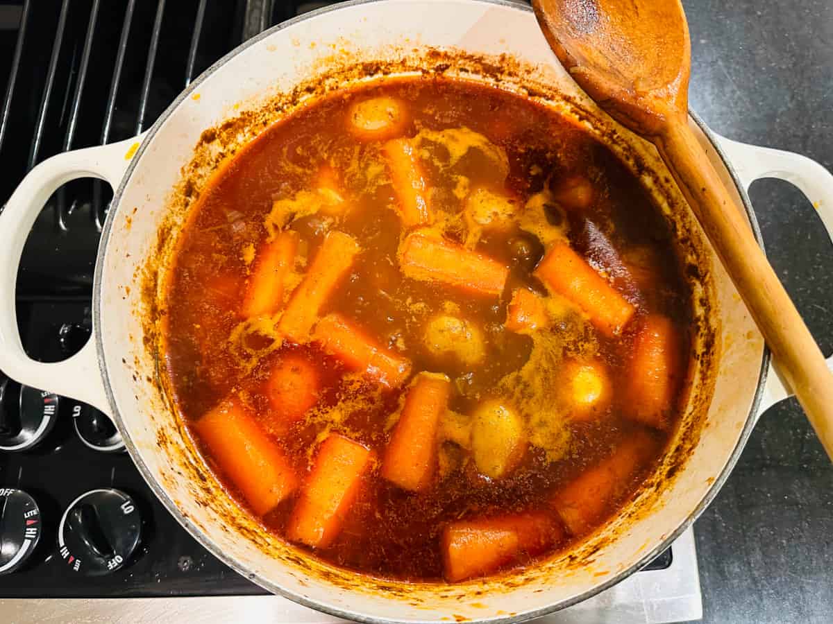 Irish stew simmering in a white pot with a wooden spoon.