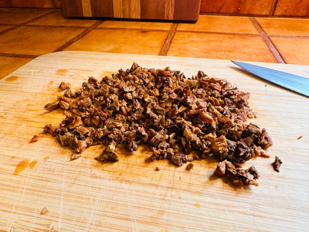 Roughly chopped porcini mushrooms on a light colored cutting board next to a knife.