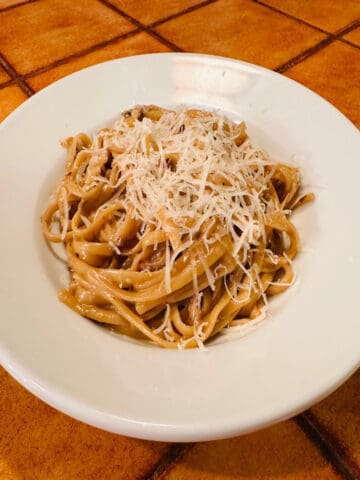 Porcini pasta sprinkled with shredded parmesan in a white bowl on a terra cotta colored tile counter.