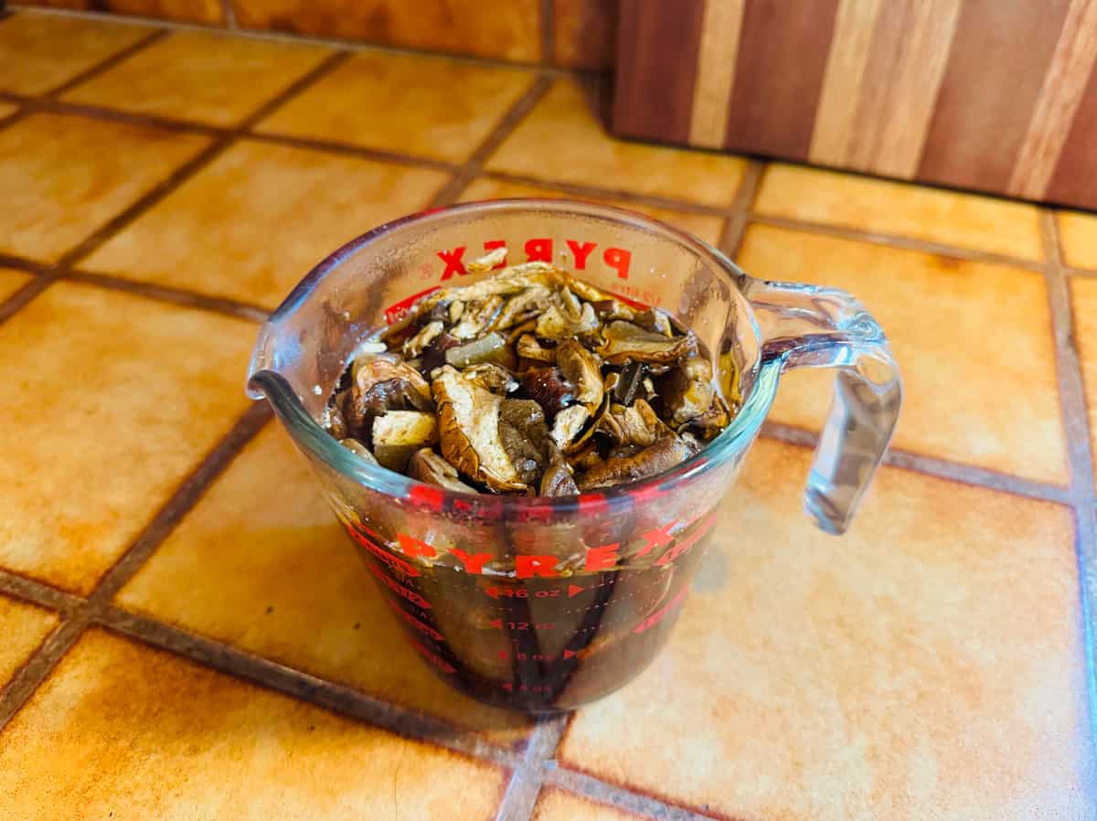 Dried porcini mushrooms soaking in hot water in a glass pyrex measuring cup with red markings.