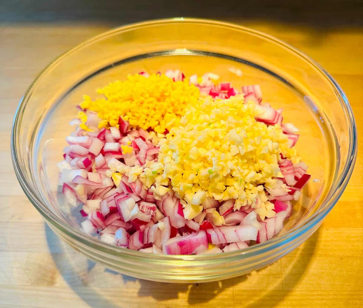 Diced red onion with minced garlic and ginger in a glass bowl.