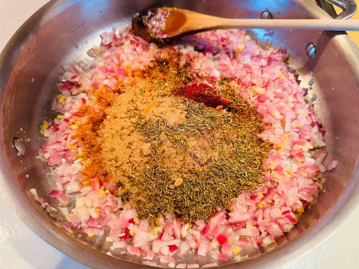 Spices added to cooked onion, garlic, and ginger in a steel saute pan with a wooden spoon.