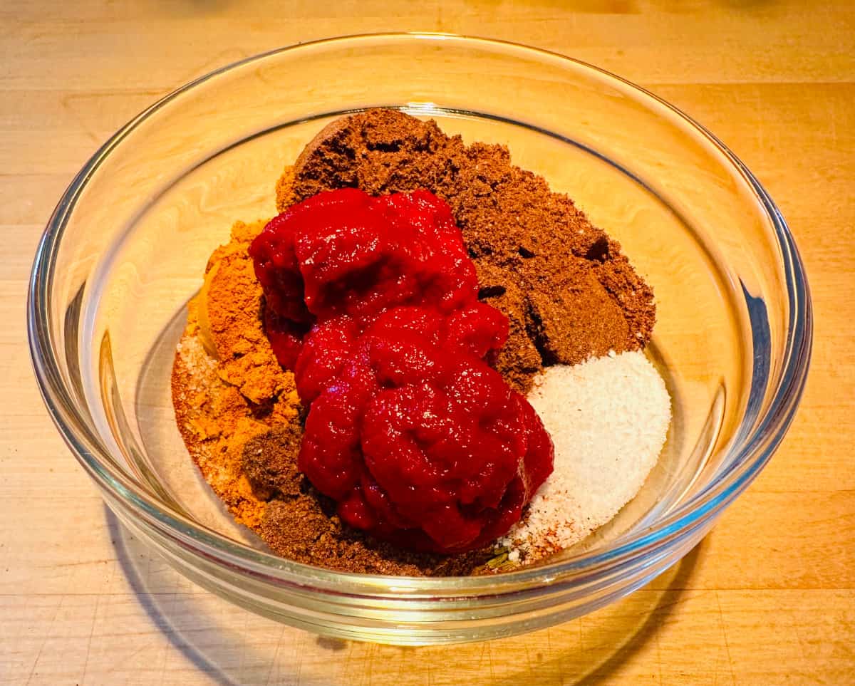 Spices and tomato paste measured out into a glass bowl.
