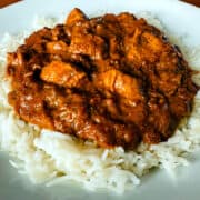 "Butter" chicken on a bed of basmati rice on a white plate.