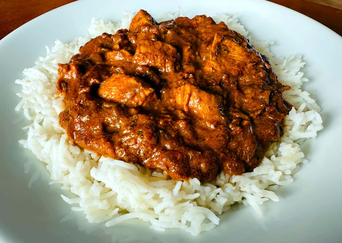 "Butter" chicken on a bed of basmati rice on a white plate.