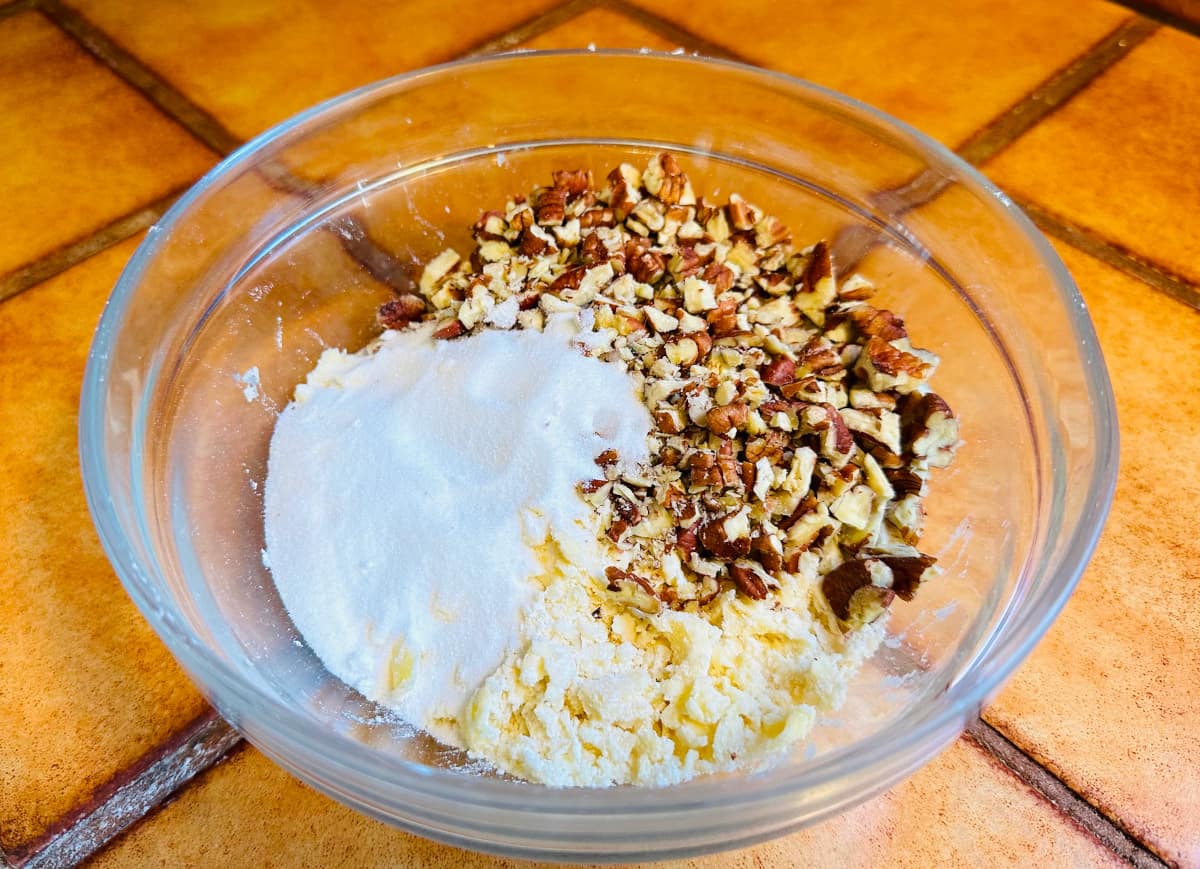 Sugar, chopped pecans, and small clumps of butter and flour in a glass bowl.