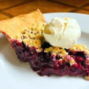 Slice of blueberry crumble pie served a la mode on a white plate.