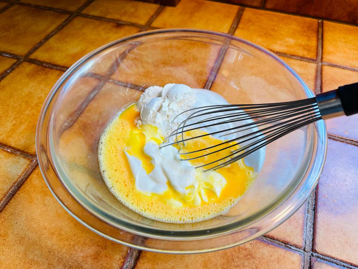 Sour cream, beaten egg, sugar, and flour in a glass bowl with a metal whisk.