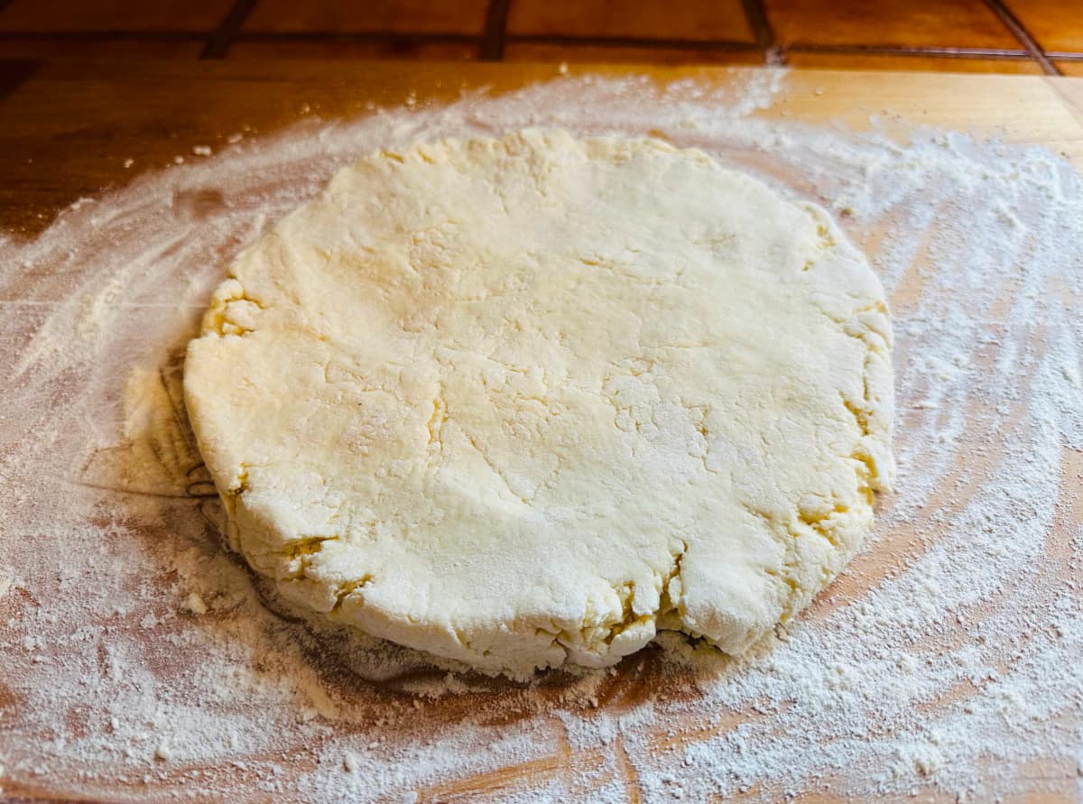 Biscuit dough patted into a flat round on a floured wooden board.