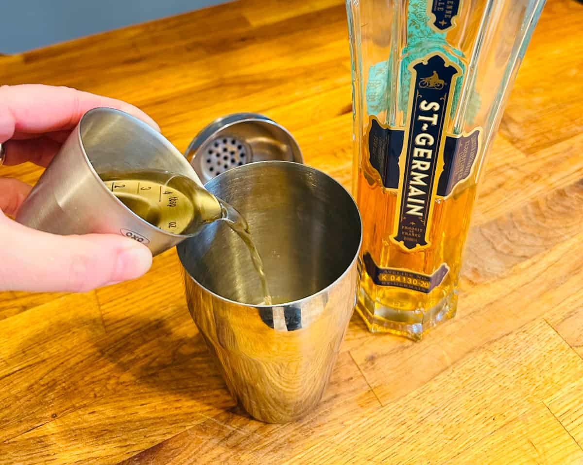 St. Germain being poured from a metal measuring cup into a cocktail shaker.