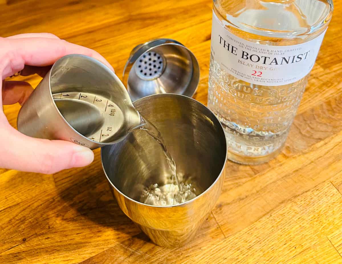 Gin being poured from a metal measuring cup into a cocktail shaker.