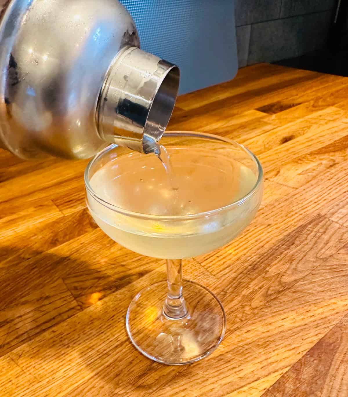 Elderflower martini being poured from a frosty cocktail shaker into a small coupe glass.