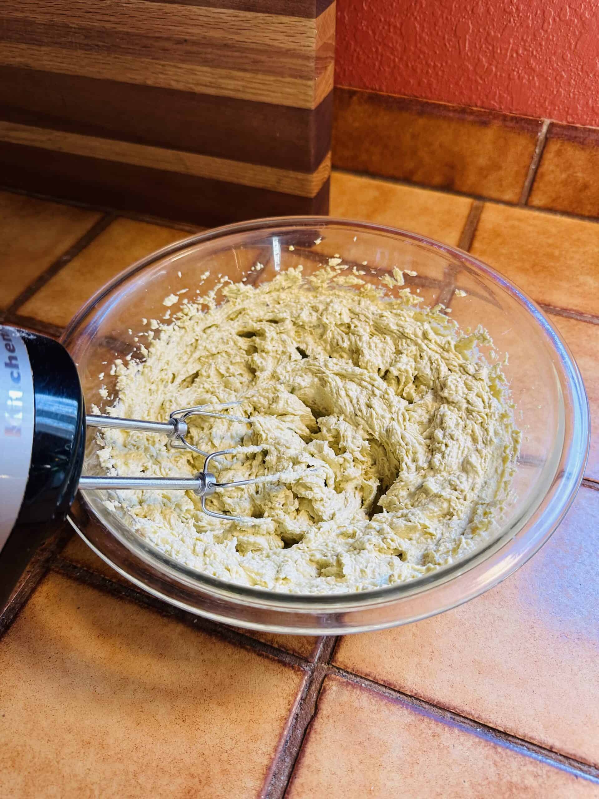 Pistachio buttercream in a glass bowl with an electric mixer.