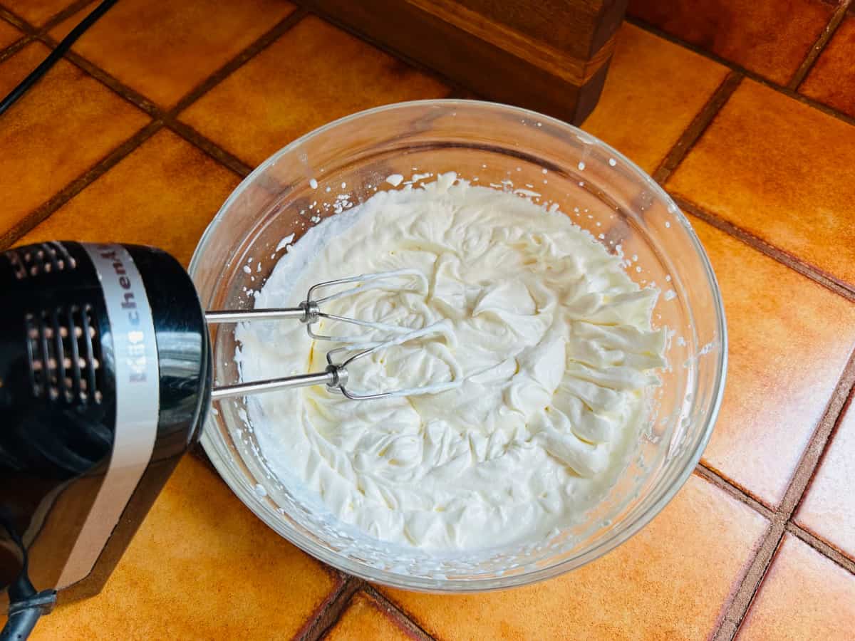 Whipped cream in a glass bowl with an electric mixer.