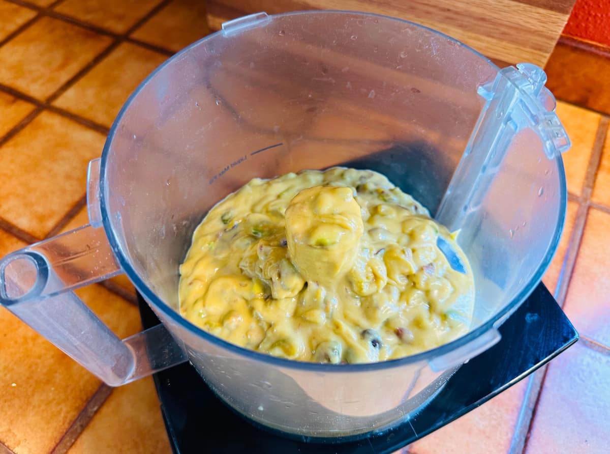 Pistachio pastry cream in the bowl of a food processor.