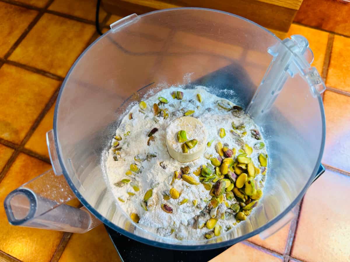 Flour and pistachios nuts in the bowl of a food processor.