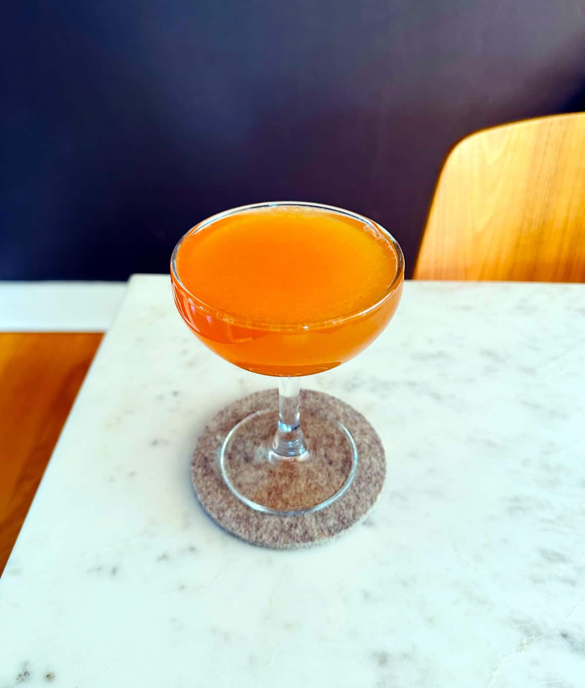 Wild Kentuck Buck cocktail in a coupe glass sitting on a gray coaster on top of a marble table.