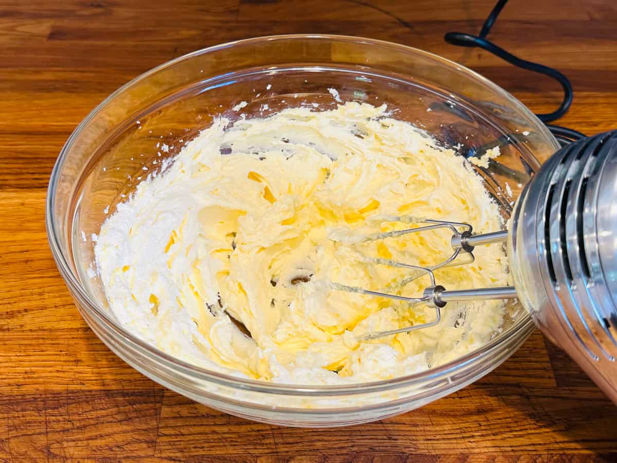 Creamed butter and sugar in a glass bowl with a silver handheld electric mixer.