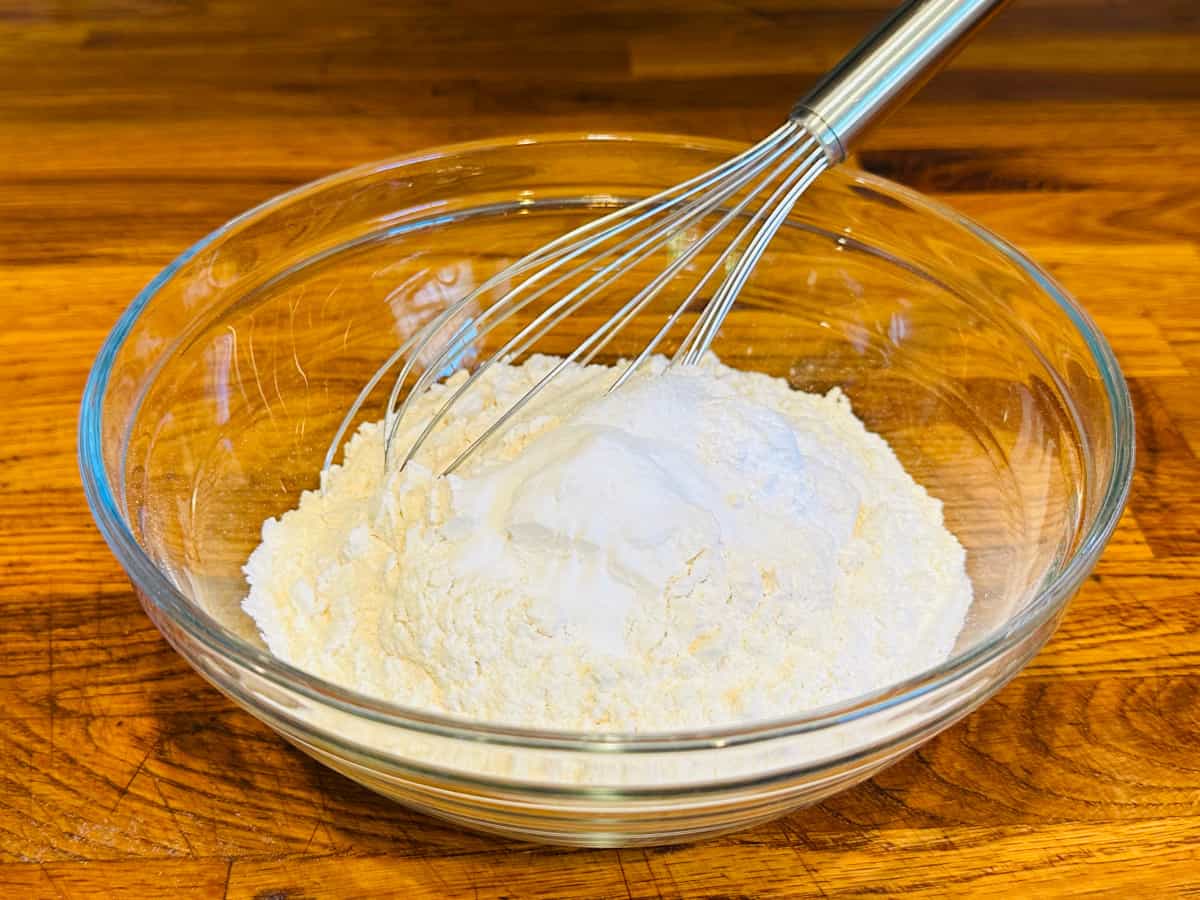 Flour and other dry ingredients in a glass bowl with a steel whisk.