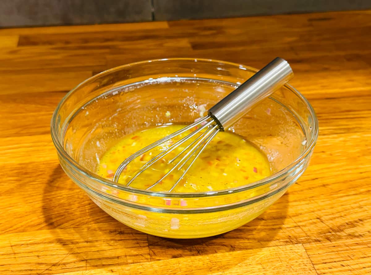 Yellow liquid flecked with chopped shallots in a small glass bowl with a tiny steel whisk.